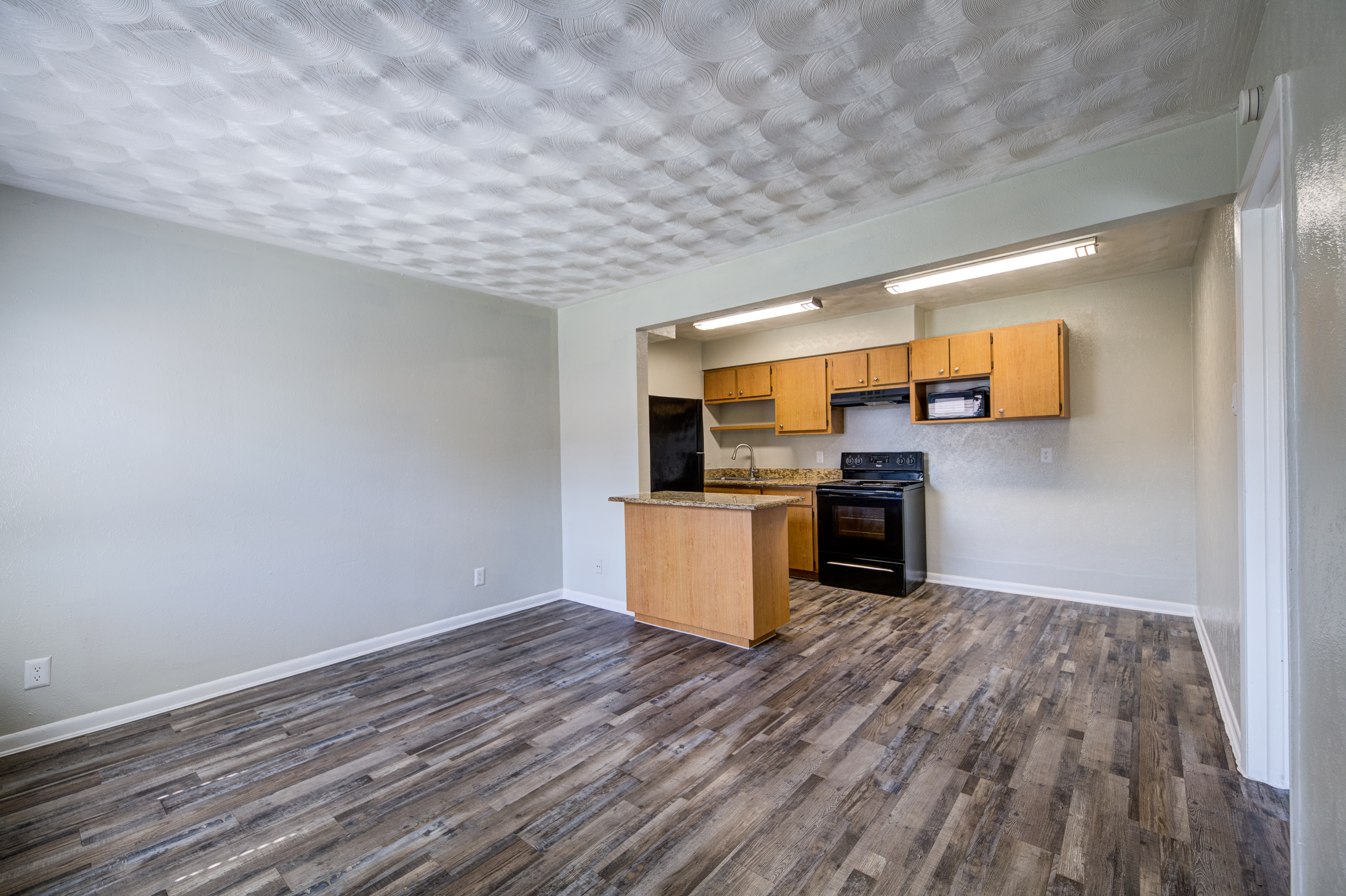 Living room with grey vinyl plank floors and an open kitchen at Oakwood Crest Apartments